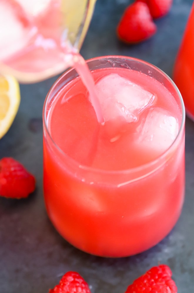 Pouring raspberry lemonade into a glass filled with ice