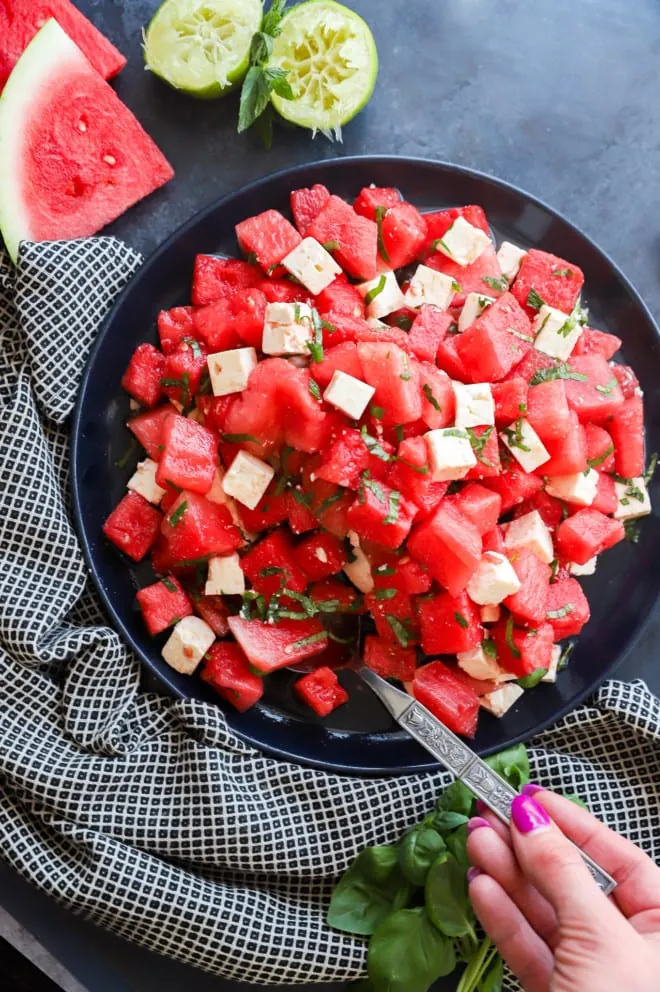 Hand holding a spoon to serve a summer salad from a platter