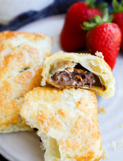 Nutella puff pastry pie cut in half with nuts on plate with strawberries