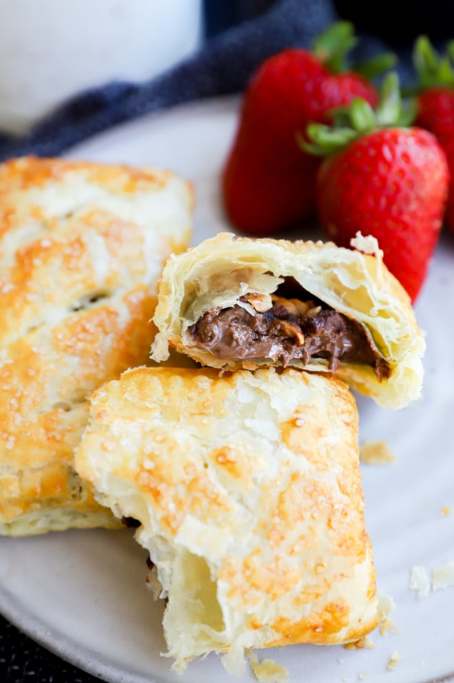 Nutella puff pastry pie cut in half with nuts on plate with strawberries