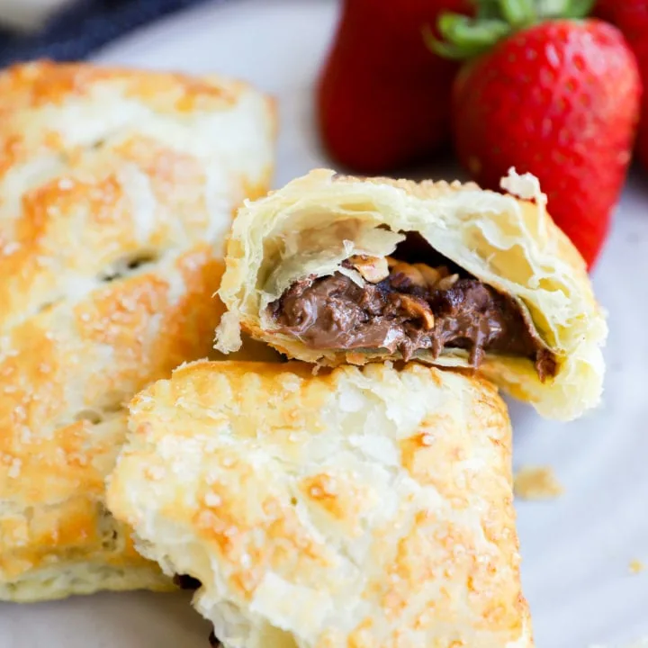Nutella puff pastry pie cut in half with nuts on plate with strawberries