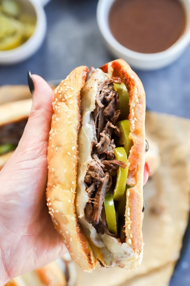 Hand holding a french dip sandwich with peppers on it