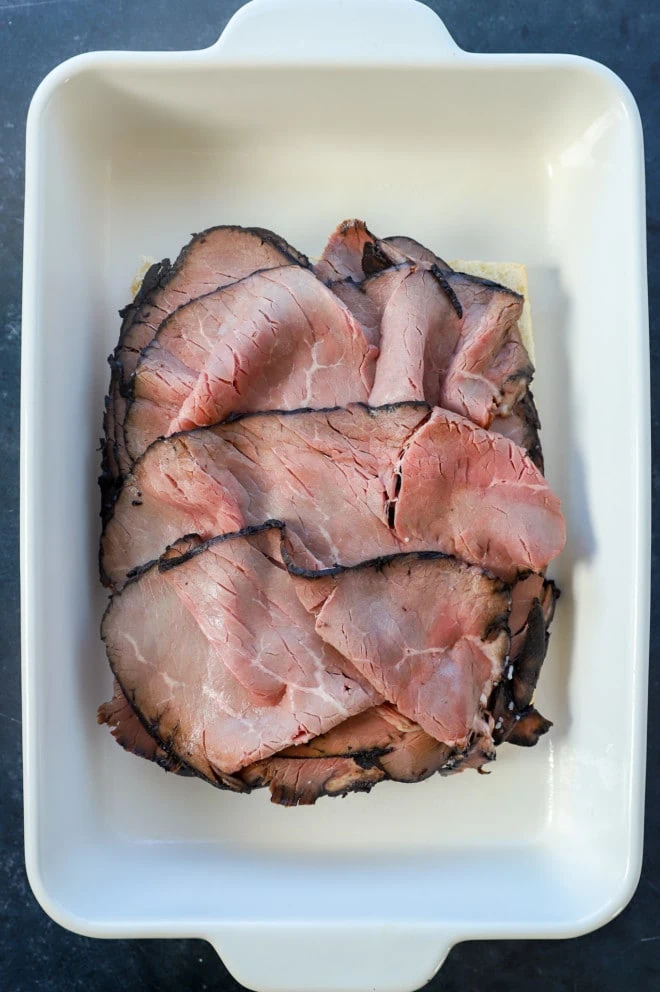 roast beef on top of rolls in baking dish