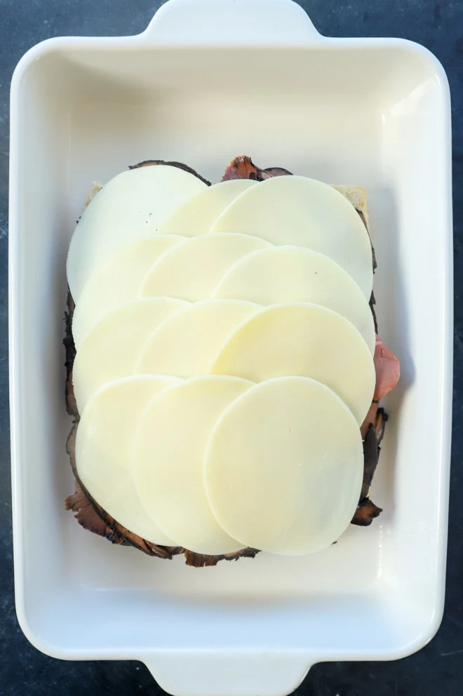 cheese on top of roast beef on rolls in a baking dish