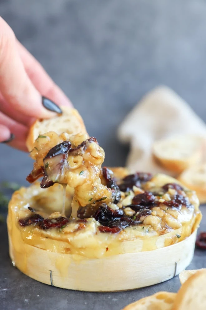 Dipping bread into gooey baked camembert with cranberries and walnuts