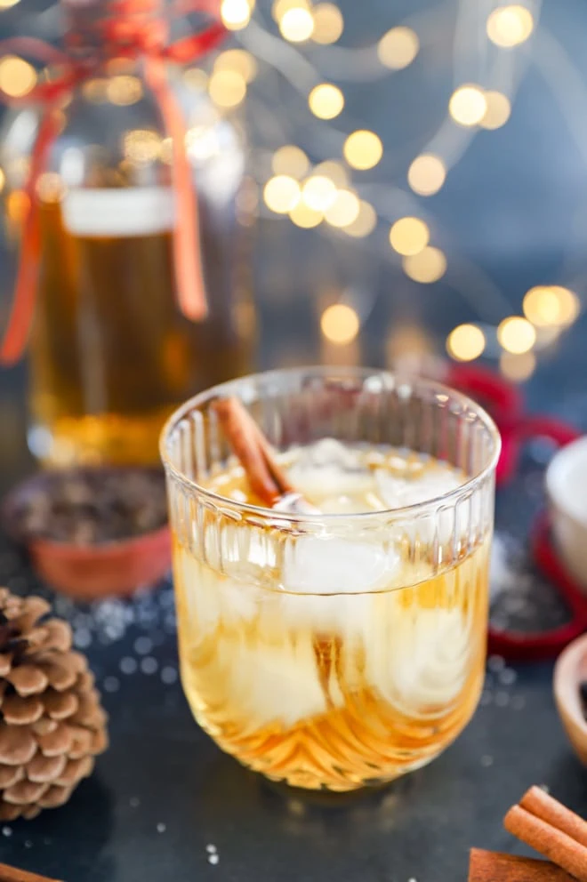 Twinkling lights in the background of a holiday cocktail in a glass with cinnamon stick