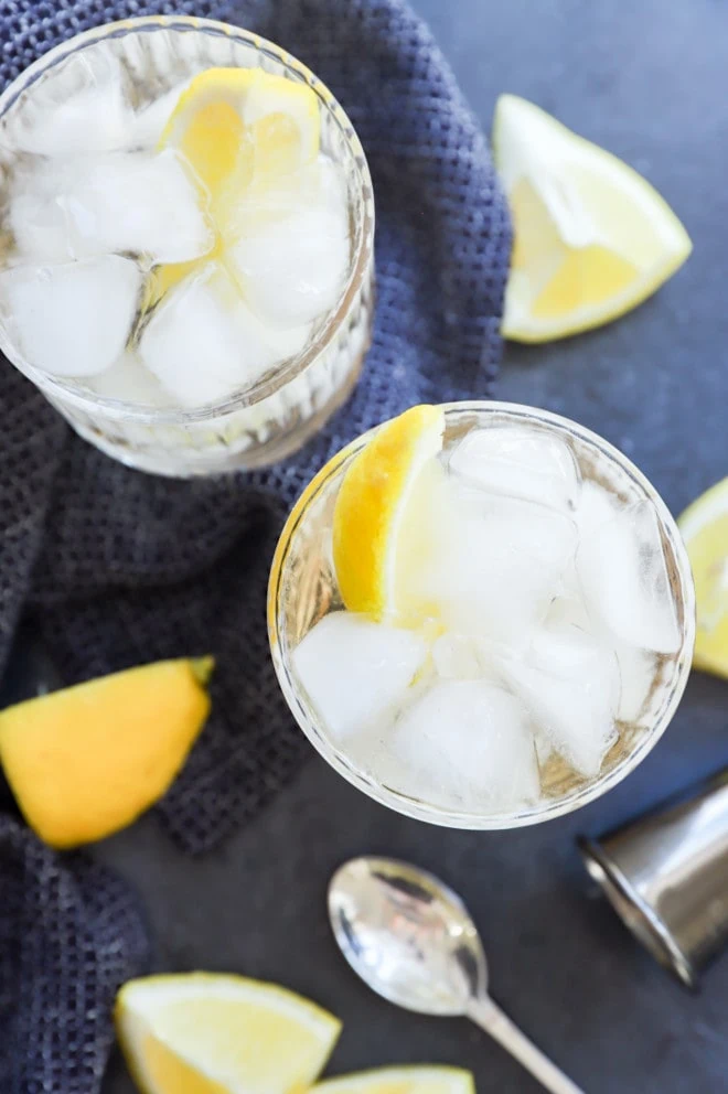 two cocktails in glasses with lemon wedges and jigger