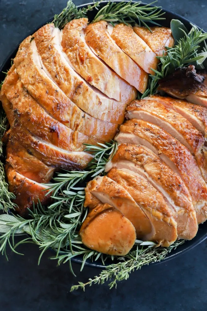 sliced thanksgiving smoked turkey breast on a plate with herbs