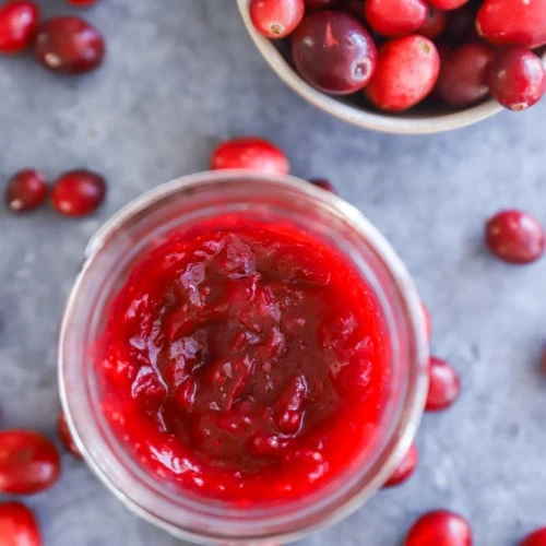cranberry jam in a mason jar with a bowl of fresh cranberries