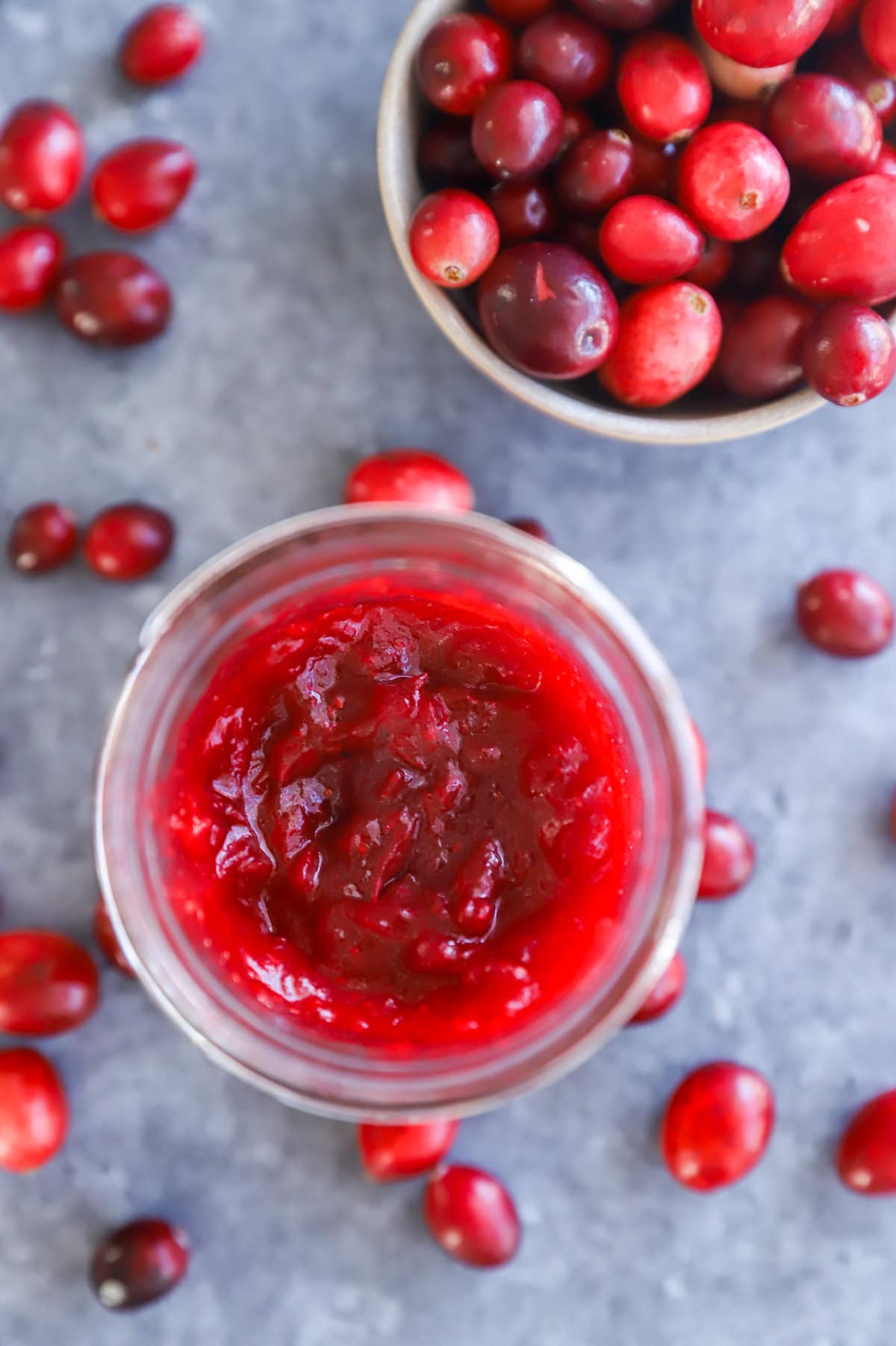 cranberry jam in a mason jar with a bowl of fresh cranberries