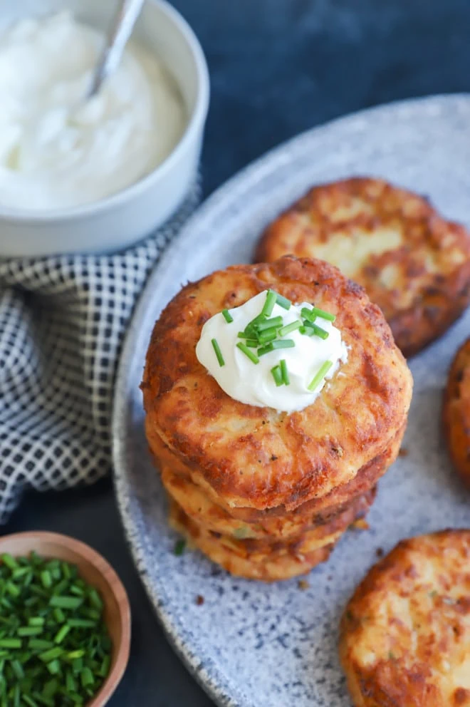 fried pancakes in a pile on a platter with sour cream and chives
