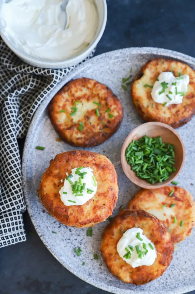 mashed potato pancakes with fresh chives and sour cream on grey platter with linen