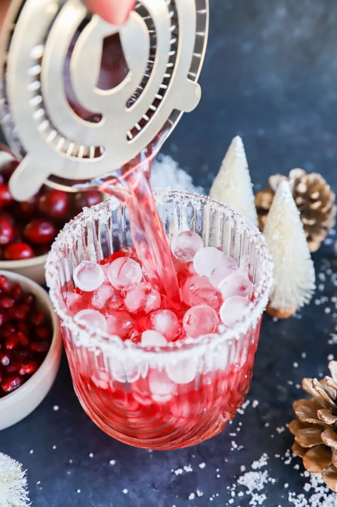 Pouring a cranberry pomegranate cocktail into a glass with ice
