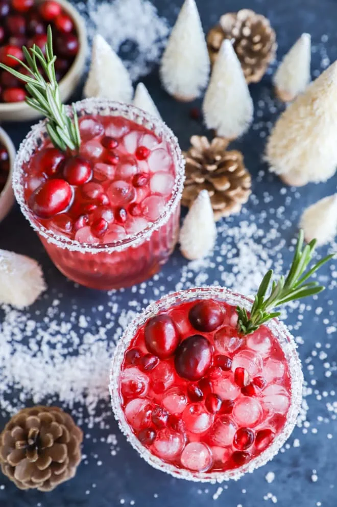 Two holiday cocktails in glasses with ice and fresh fruit