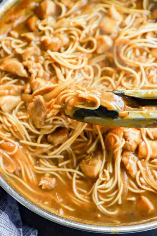 Tongs lifting up curry udon from skillet