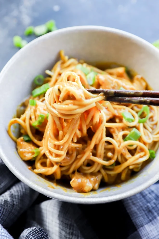 Chopsticks lifting up noodles from a bowl with chicken