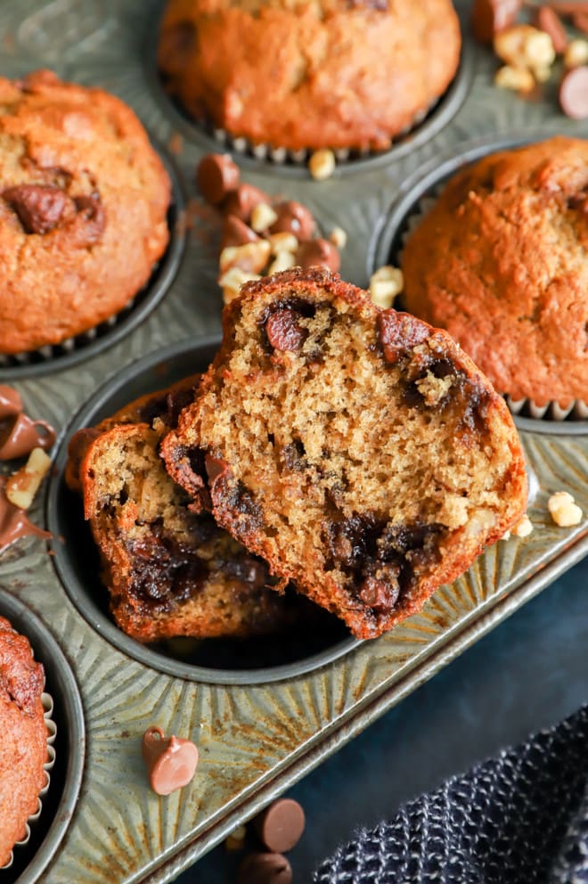 A baked morning treat cut in half showing chocolate chips and nuts in muffin tin