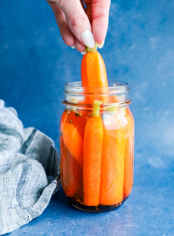hand pulling out a quick pickled carrot from a jar