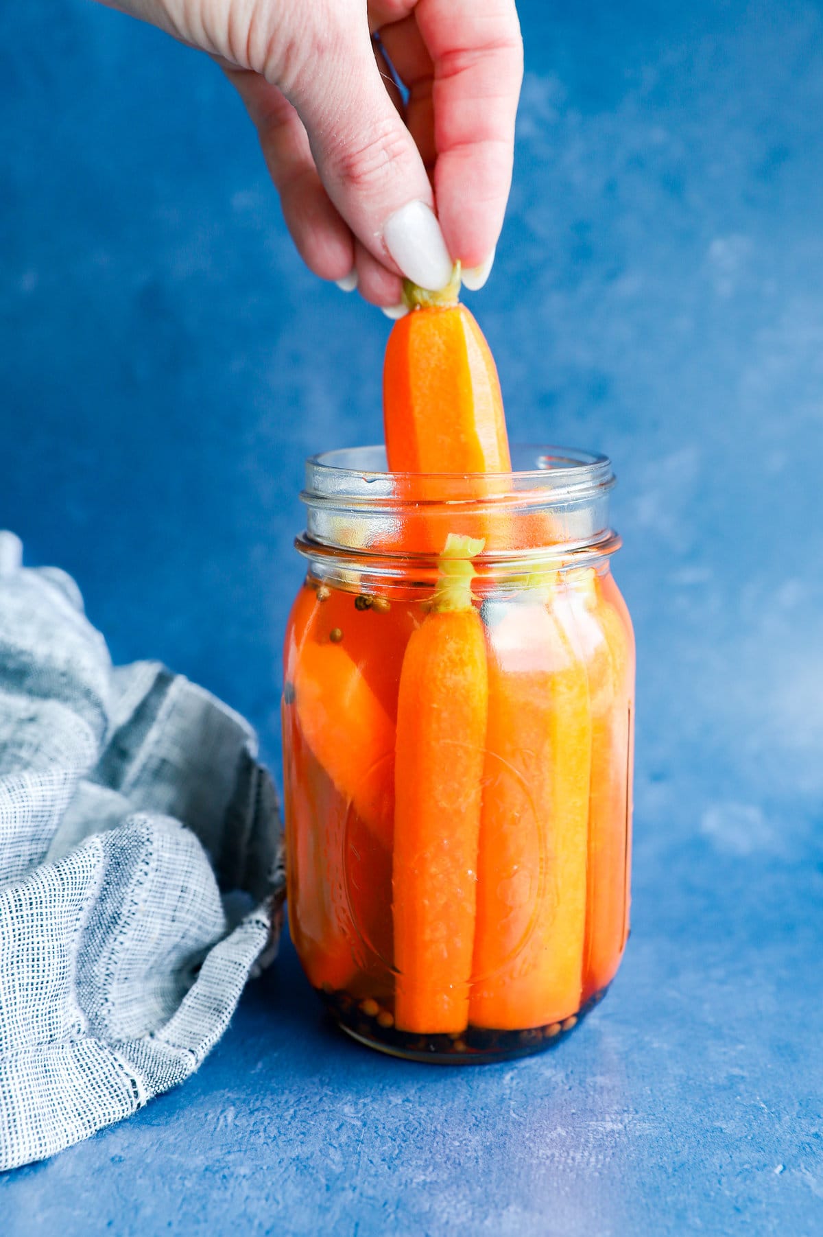 hand pulling out a quick pickled carrot from a jar