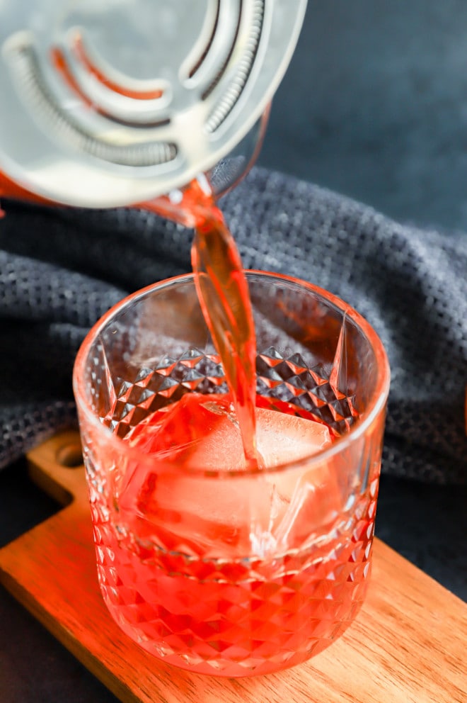 Pouring aperol negroni into a cocktail glass
