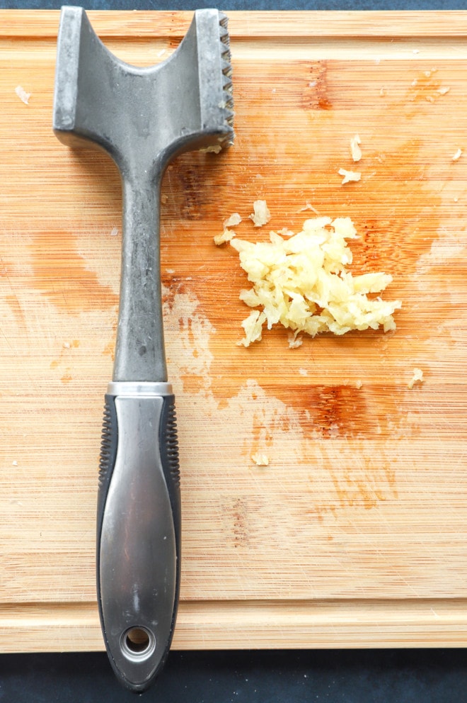 Mashed garlic on a cutting board with meat tenderizer