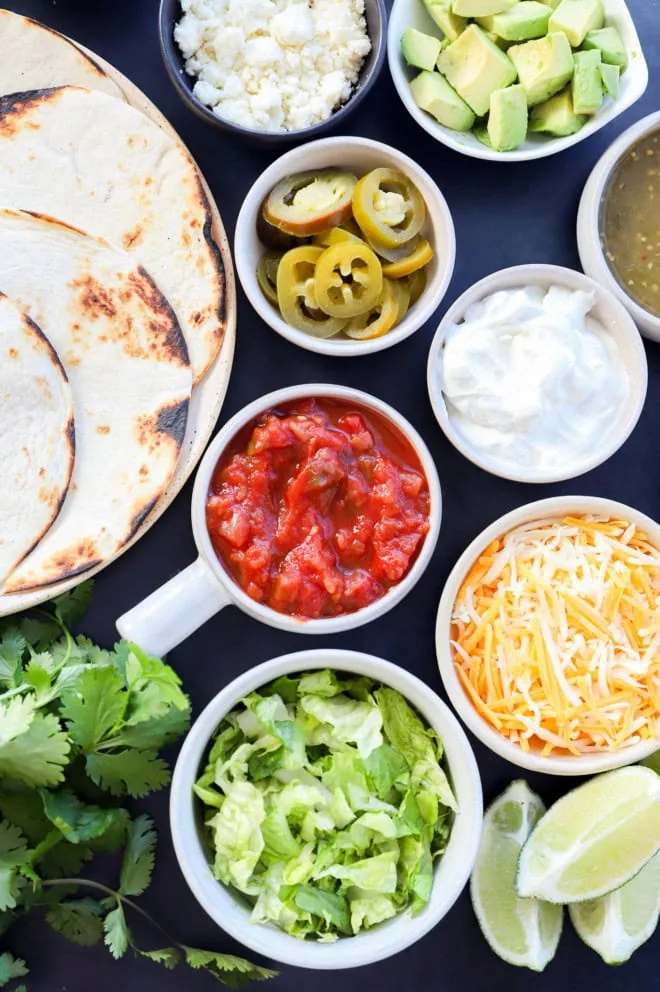 Bowls full of different salsas, vegetables, cheeses, dips, and tortillas