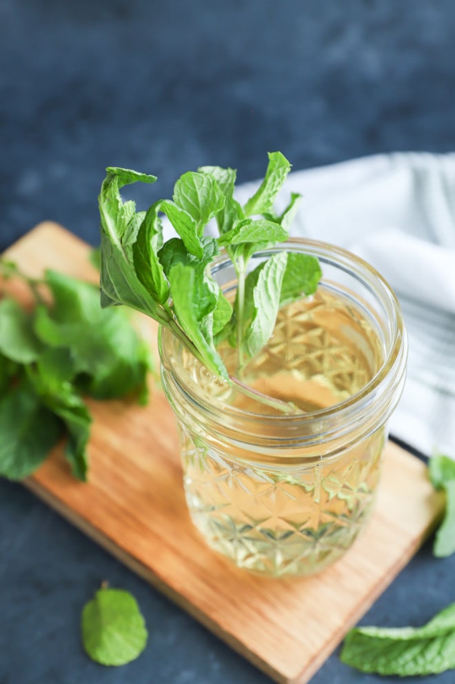 Fresh mint in a cup of mint simple syrup with mint leaves all around and cutting board