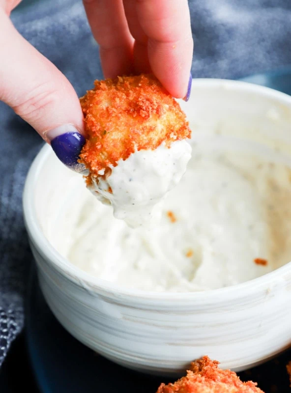 hand holding potato cheese ball dipped in creamy sauce