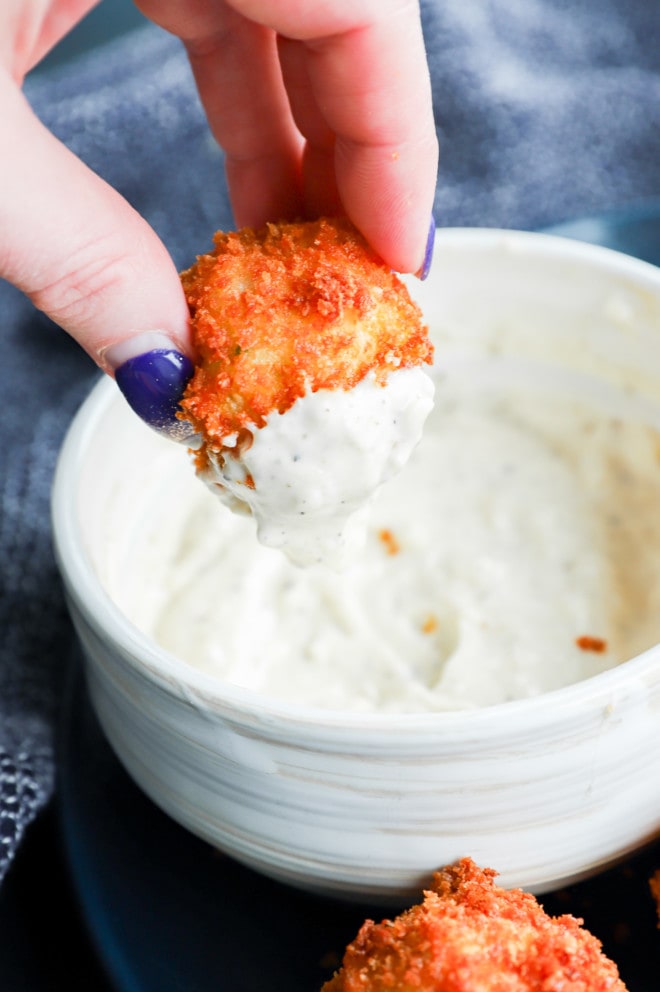 hand holding potato cheese ball dipped in creamy sauce