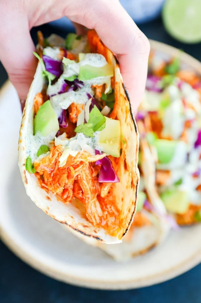 hand holding buffalo chicken taco with ranch on top