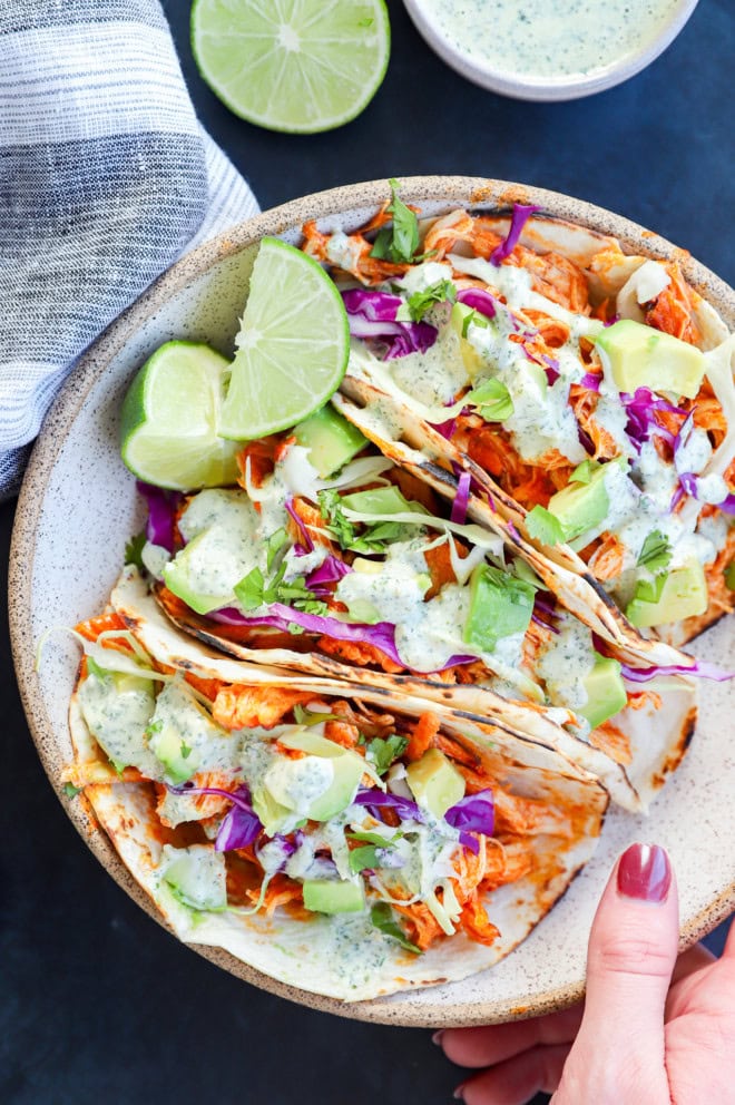 hand holding bowl of spicy tacos with fresh limes