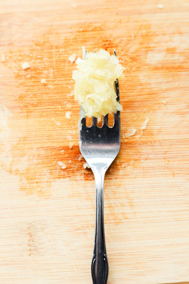 mashed garlic on a fork on a cutting board