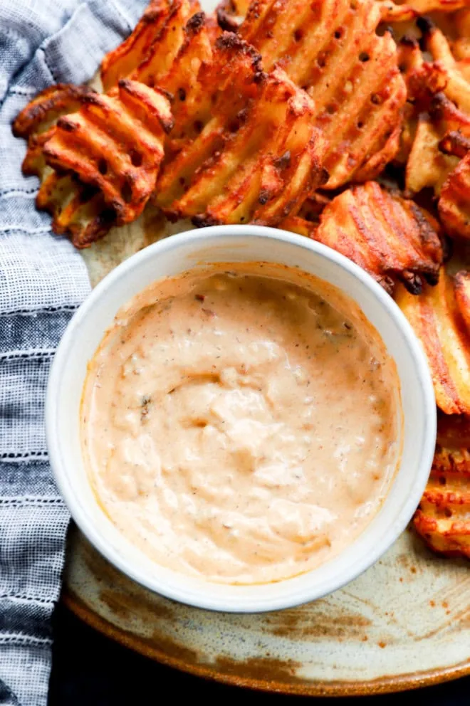 Bowl of chipotle aioli with waffle fries on platter with linen napkin