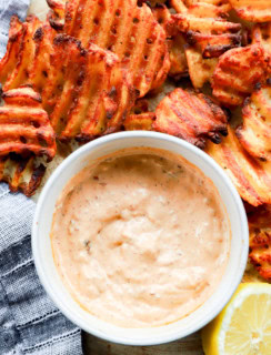 Image of a dipping sauce with fried potatoes and a lemon half on a platter with a linen napkin