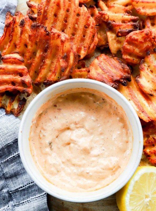 Image of a dipping sauce with fried potatoes and a lemon half on a platter with a linen napkin