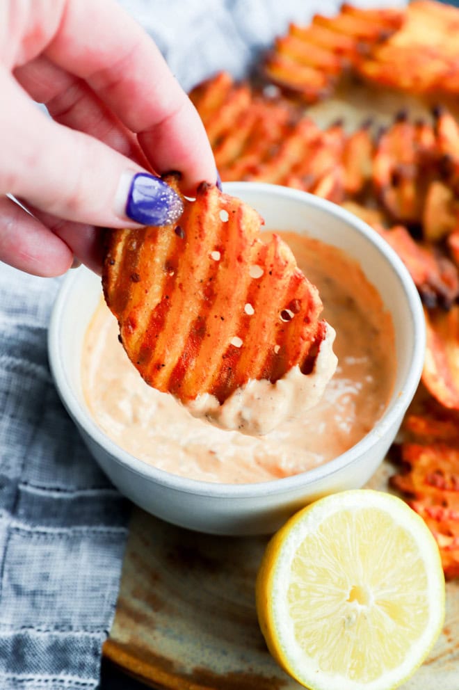 hand holding fry dipping into the chipotle aioli in a bowl