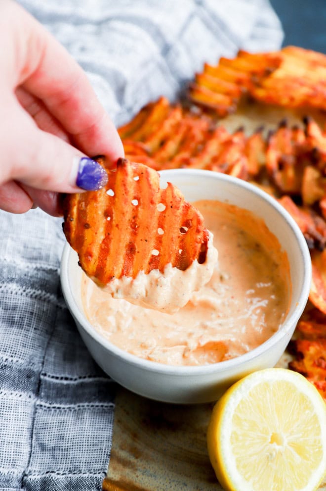 Hand holding fry dipped into a creamy sauce