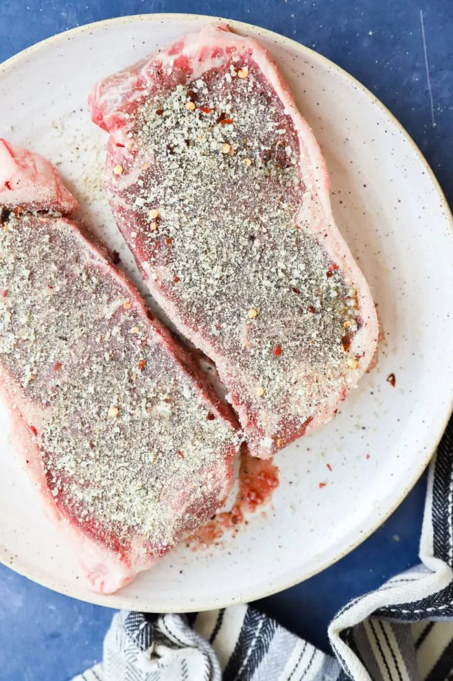 new york strip steak rubbed with steak rub on plate before cooking