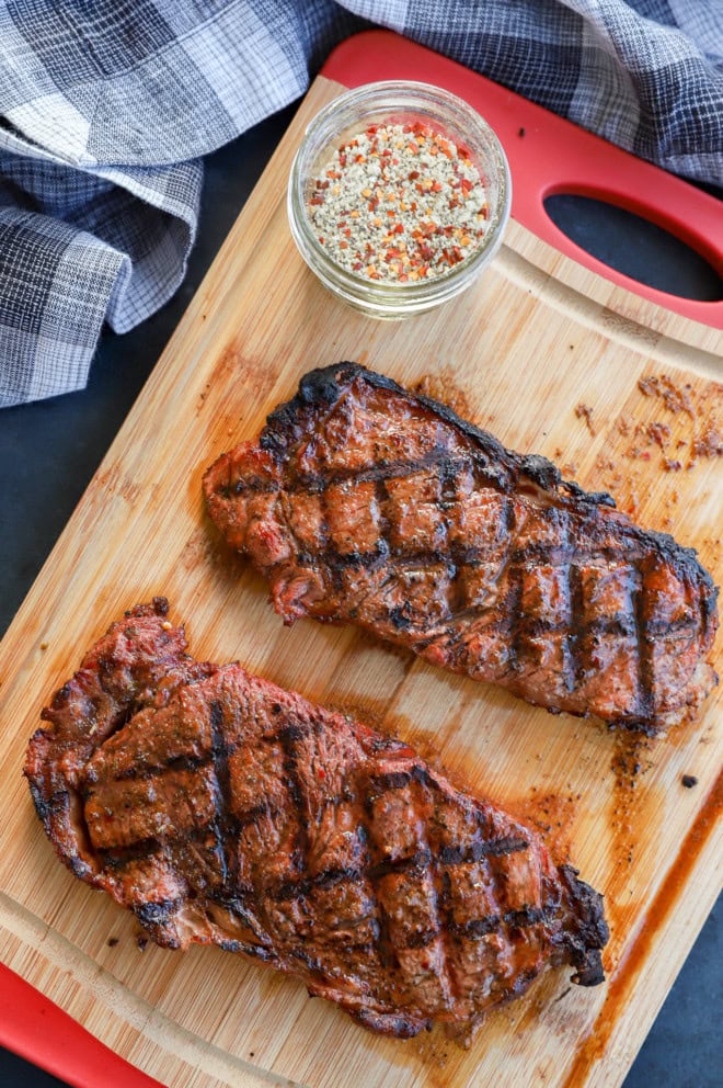 new york strip steaks on cutting board with steak rub and crosshatch grill marks
