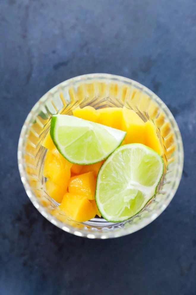 lime wedges and mango chunks in a glass before muddling them together