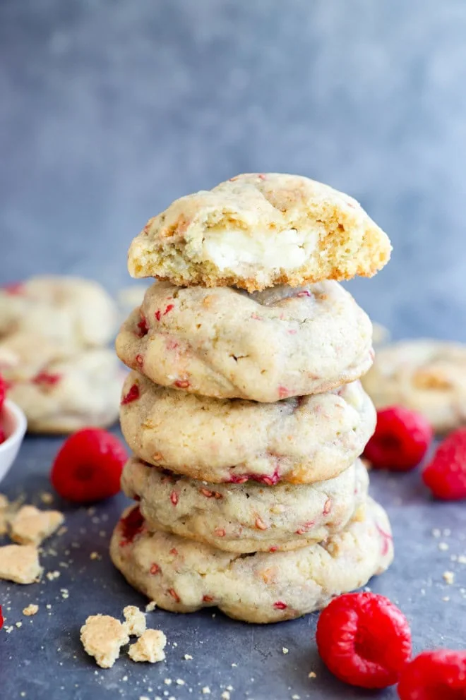 bite taken out of raspberry cheesecake cookie on a pile of cookies with fresh raspberries