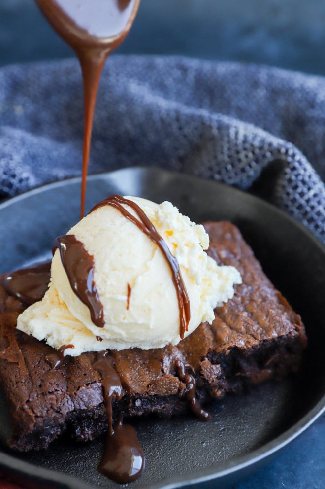 drizzling hot fudge sauce on a sizzling brownie