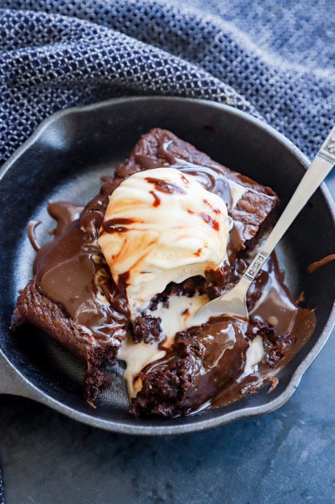 Fork with hot fudge sauce and chocolate baked treat in hot skillet