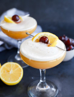 Glasses of disaronno sour cocktails with lemon and bowl of cherries