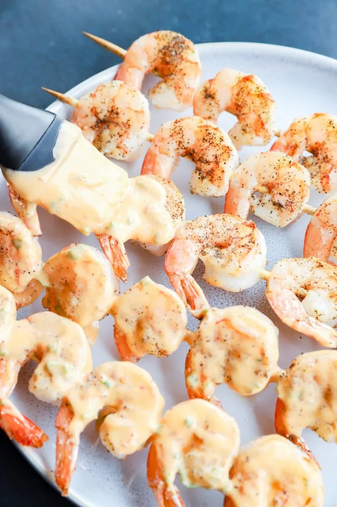Brushing bang bang sauce onto grilled shrimp skewers