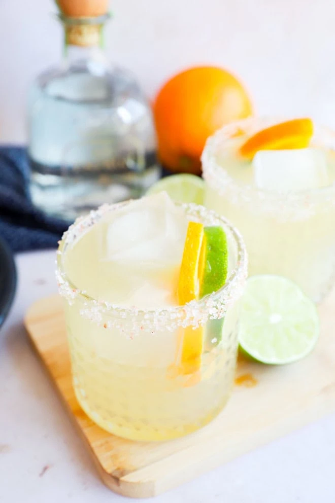 Two patron margaritas in glasses with a patron bottle in the background