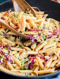 lifting pasta salad out of a serving bowl with woodn spoons