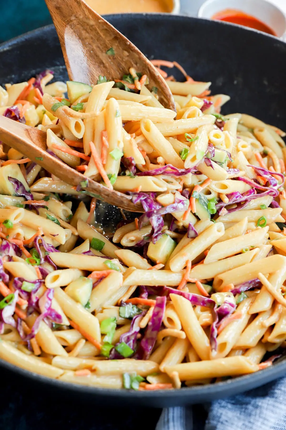 lifting pasta salad out of a serving bowl with woodn spoons
