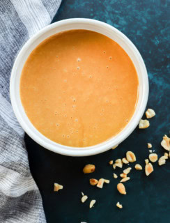 thai peanut salad dressing in a bowl with chopped peanuts around it