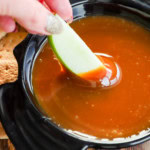 hand dipping an apple slice in caramel apple dip in a bowl